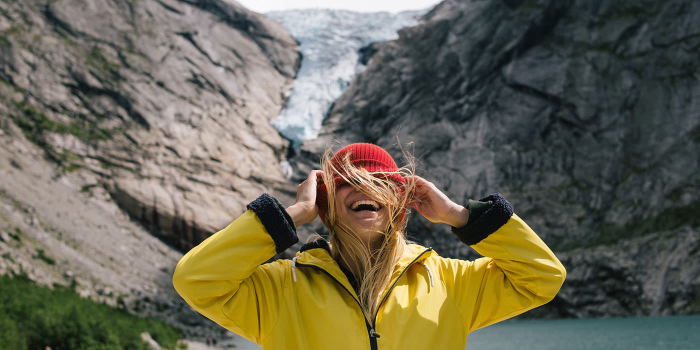 Woman in a yellow jacket and red hat by a glacier lake in the Norwegian mountains – illustration for hiking maps and outdoor life