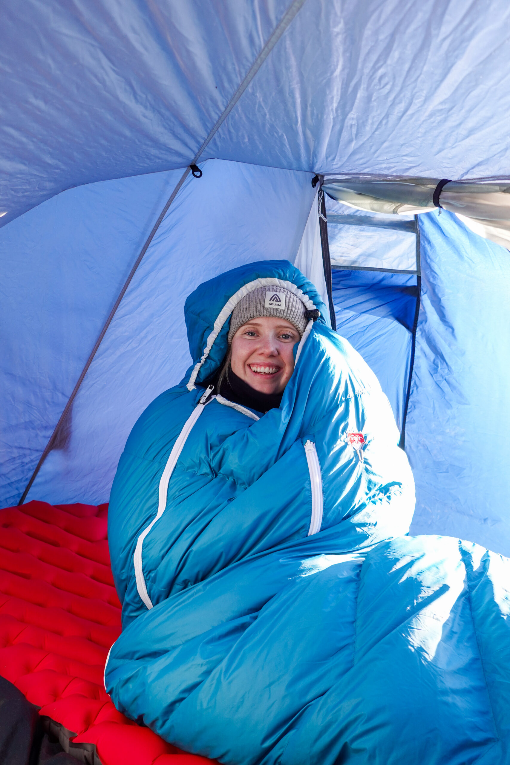 Karen Kyllesø smiler fra en blå Grüezi Bag DownWool Subzero 2.0-sovepose inne i teltet.