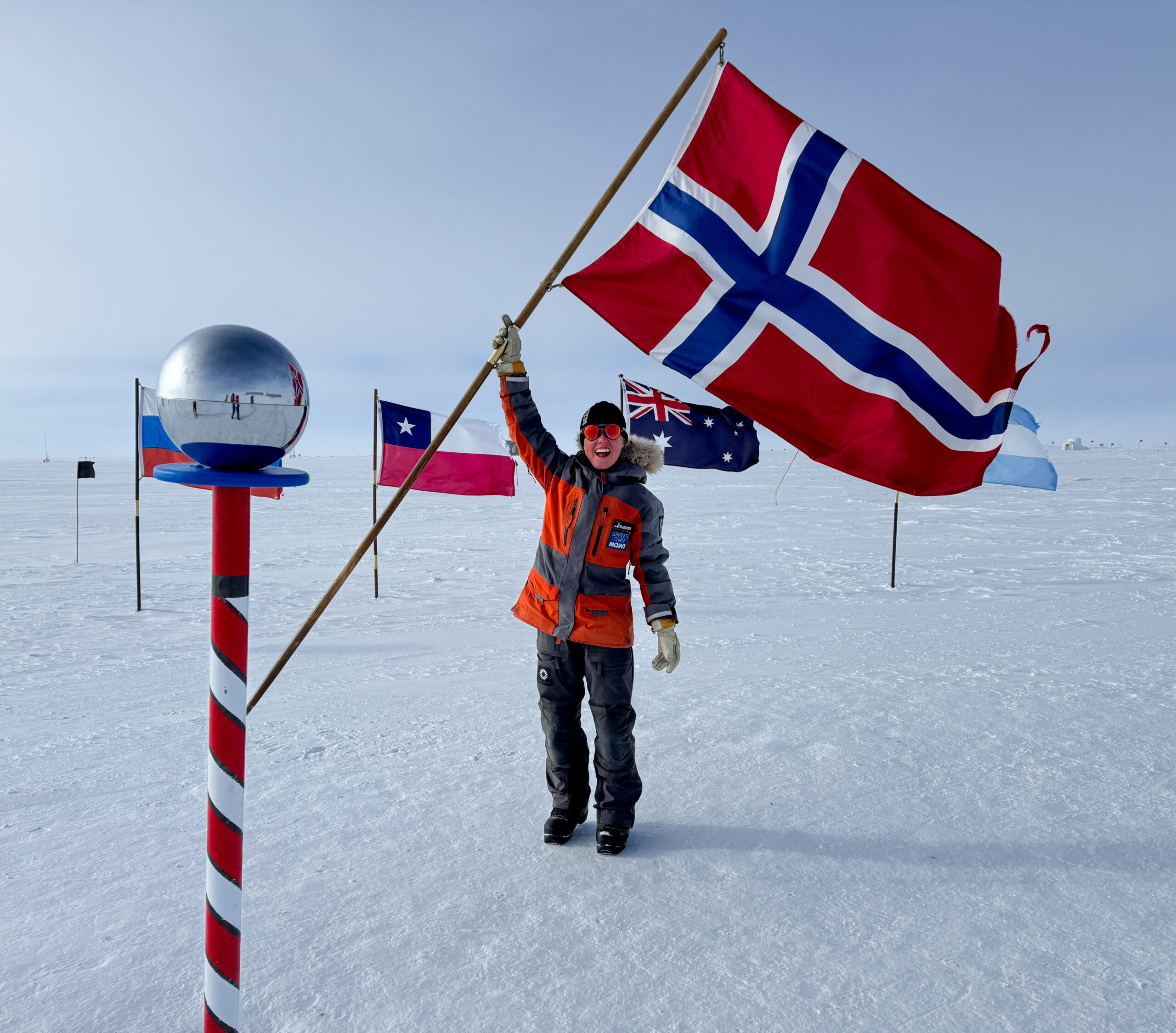 Polfarer Karen Kyllesø med norsk flagg ved en polmarkør i snølandskap.